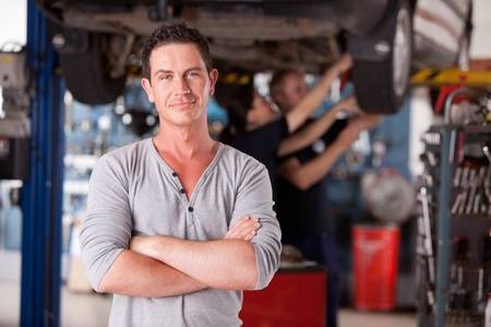 10177802 portrait of a male mechanic looking at the camera with workers in the background